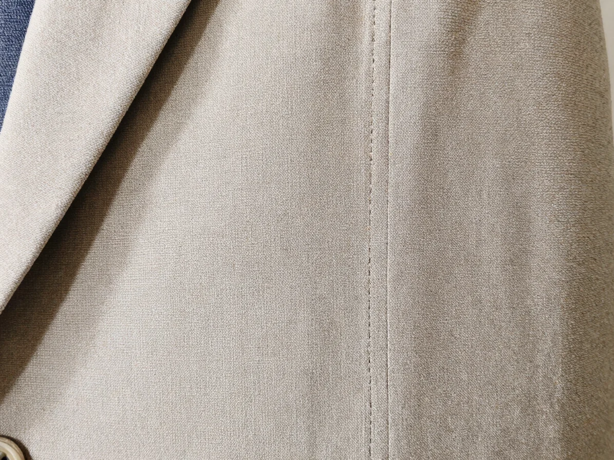 Close detail of clean woven fabric stitching on a tailored garment panel under soft neutral daylight